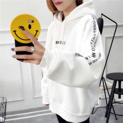 Person wearing a white hoodie with text, holding a phone with a smiley face case.