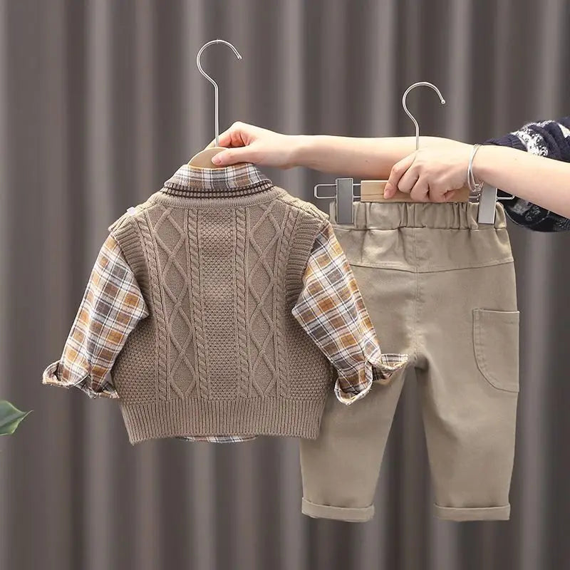 Children's clothing set with sweater vest and pants on hangers against a neutral background