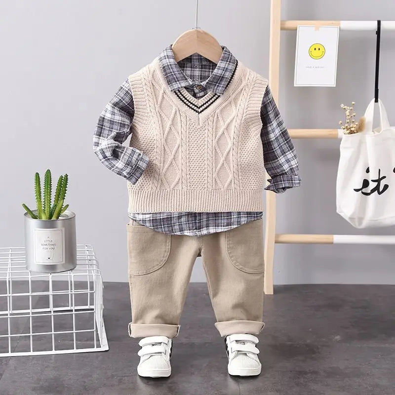Children's outfit with plaid shirt, knitted vest, and beige pants on a hanger against a neutral background.