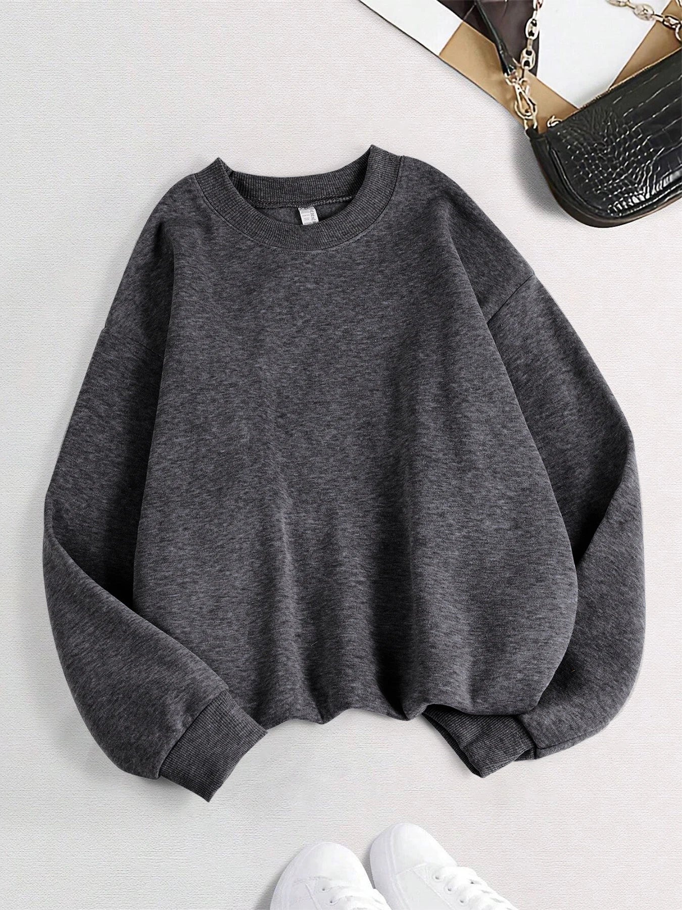 Gray sweatshirt on a light gray background with a handbag partially visible.