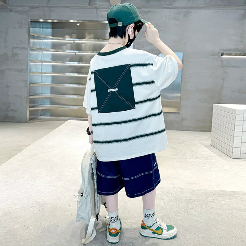 Person wearing a white t-shirt with green accents and blue shorts in an indoor setting.