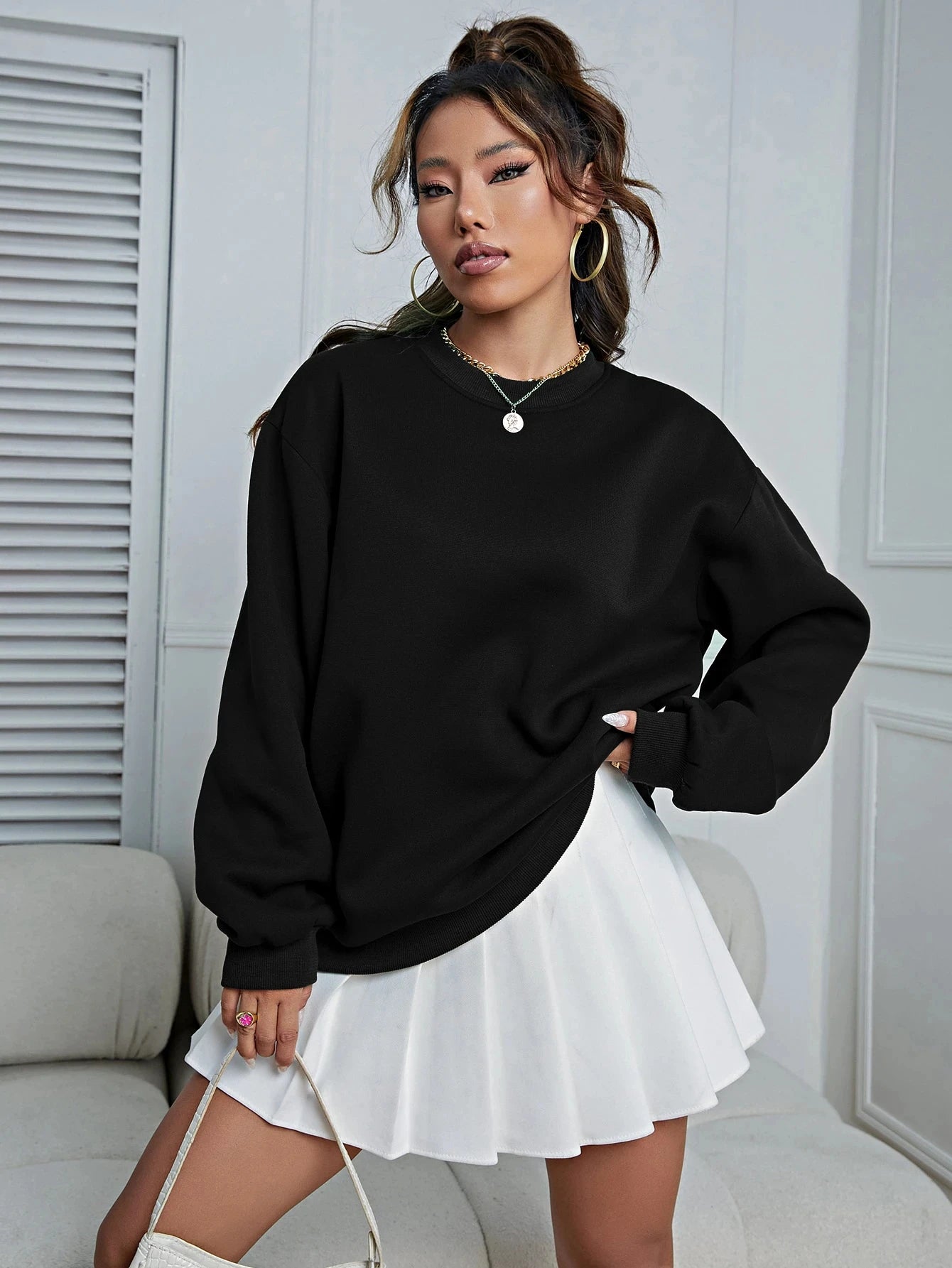 Woman wearing a black oversized sweatshirt and white skirt in a minimalistic room.