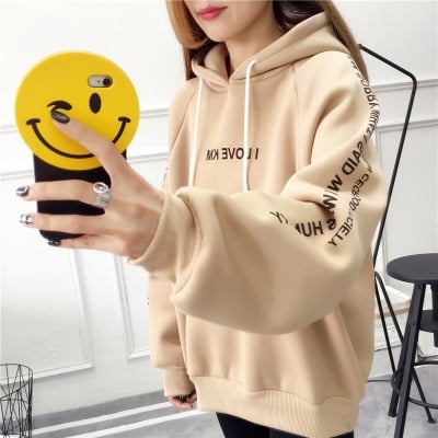 Person wearing a beige hoodie with text, holding a phone with a smiley case.