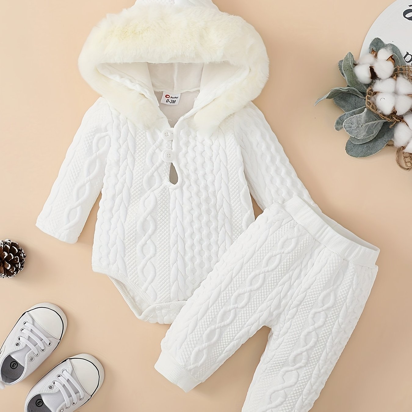 White baby outfit with cable knit pattern on a beige background